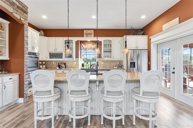 kitchen featuring white cabinetry, a kitchen island with sink, stainless steel appliances, and light stone countertops