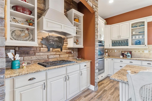 kitchen with custom range hood, light hardwood / wood-style floors, light stone countertops, and white cabinets