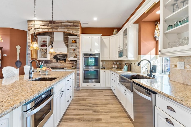 kitchen with light hardwood / wood-style flooring, stainless steel appliances, sink, pendant lighting, and white cabinetry