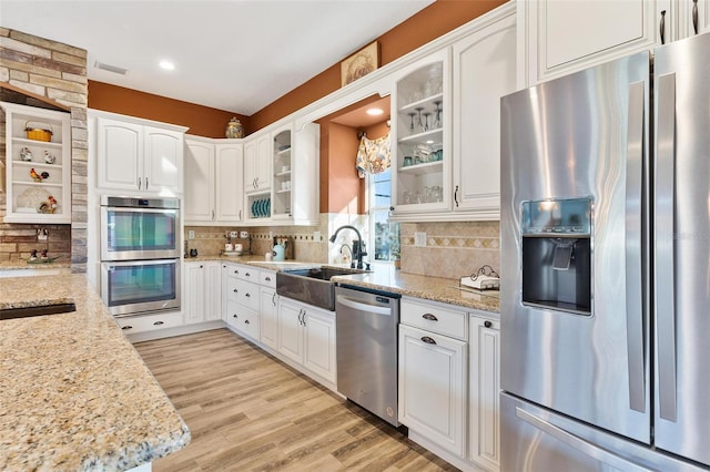 kitchen with appliances with stainless steel finishes, white cabinetry, light stone counters, and light wood-type flooring