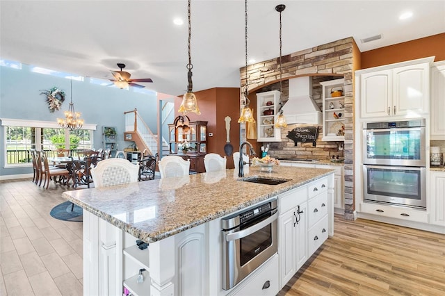 kitchen with appliances with stainless steel finishes, sink, an island with sink, hanging light fixtures, and white cabinets