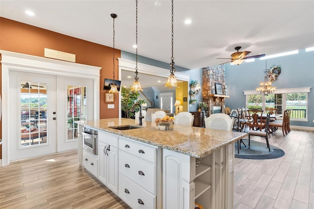 kitchen with sink, white cabinetry, ceiling fan, decorative light fixtures, and a center island with sink