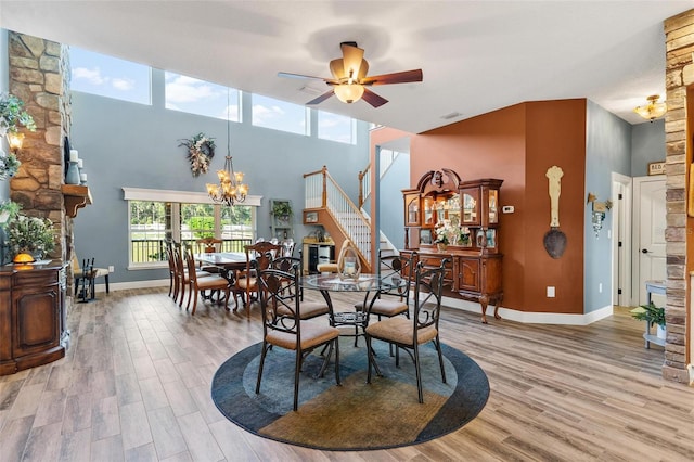 dining room with a towering ceiling, light wood-type flooring, and ceiling fan with notable chandelier