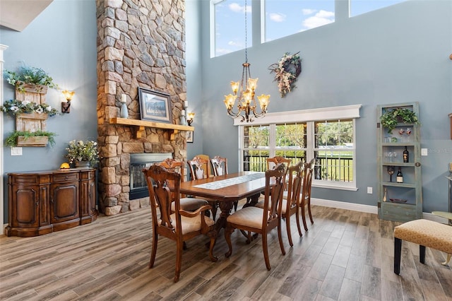 dining space with a stone fireplace, a towering ceiling, and hardwood / wood-style floors