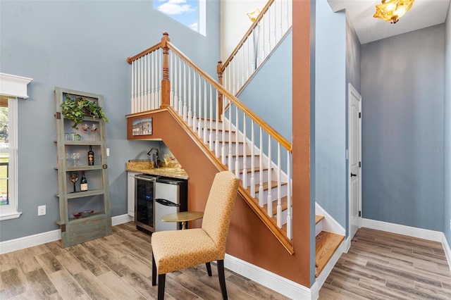 stairway featuring hardwood / wood-style flooring, indoor bar, beverage cooler, and a high ceiling