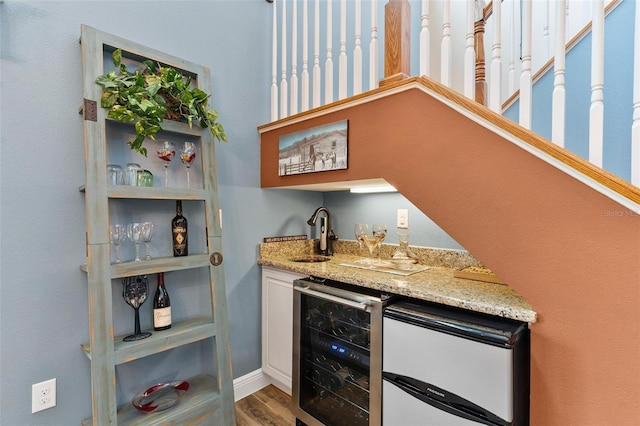 bar featuring fridge, wine cooler, sink, hardwood / wood-style floors, and light stone countertops