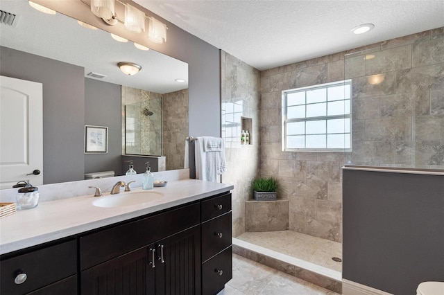 bathroom featuring vanity, a textured ceiling, tiled shower, and tile patterned floors