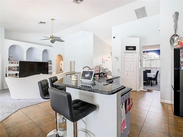 kitchen featuring ceiling fan with notable chandelier, a breakfast bar, and high vaulted ceiling