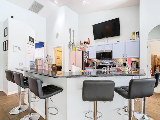 kitchen featuring white cabinets, kitchen peninsula, high vaulted ceiling, stainless steel appliances, and a breakfast bar area