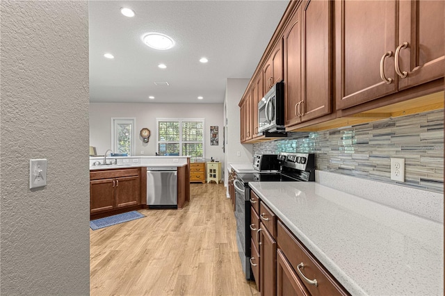 kitchen featuring kitchen peninsula, light stone countertops, stainless steel appliances, light hardwood / wood-style flooring, and sink