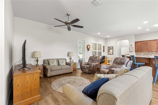 living room featuring ceiling fan, a textured ceiling, and light wood-type flooring