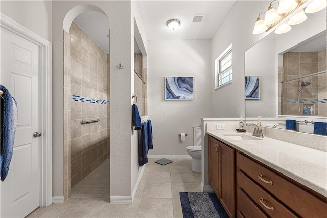 bathroom featuring vanity, tile patterned flooring, toilet, and tiled shower