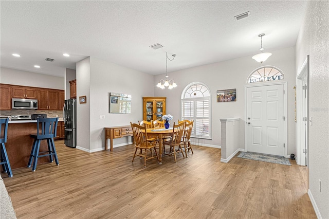 dining space with light hardwood / wood-style flooring, a chandelier, and a textured ceiling