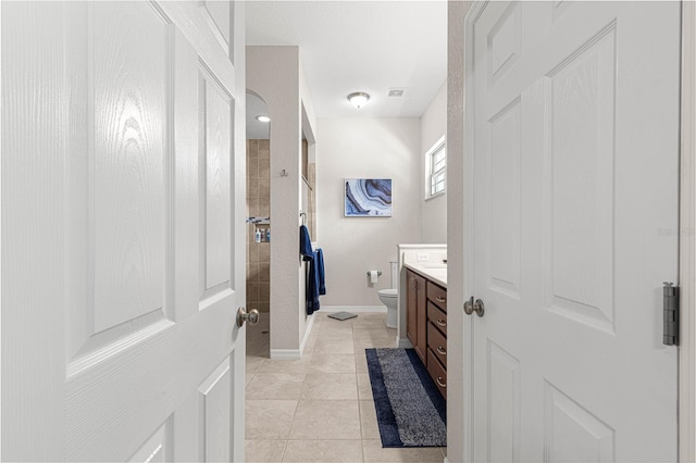 bathroom featuring tile patterned flooring, tiled shower, vanity, and toilet