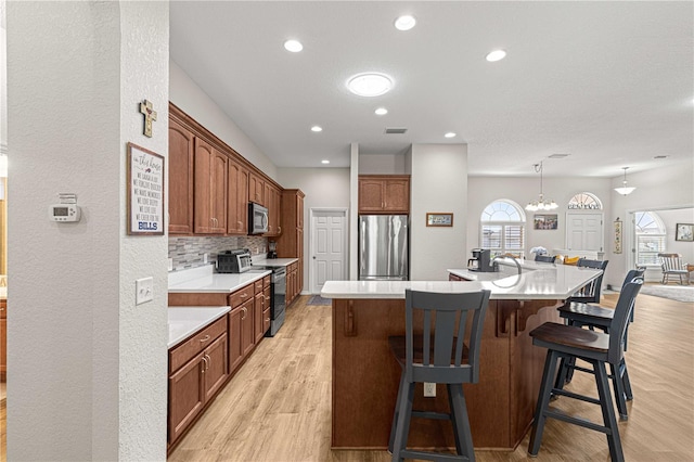 kitchen with a center island with sink, backsplash, light hardwood / wood-style flooring, appliances with stainless steel finishes, and a kitchen breakfast bar