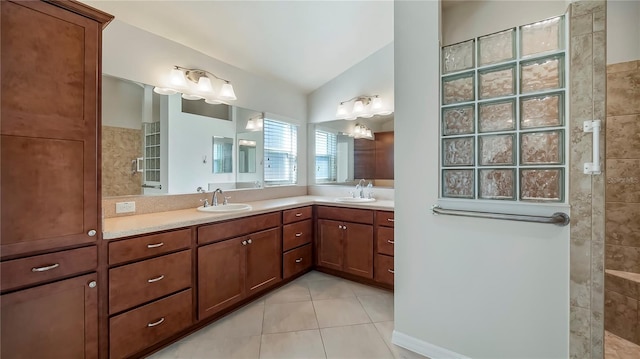 bathroom with a tile shower, lofted ceiling, vanity, and tile patterned flooring