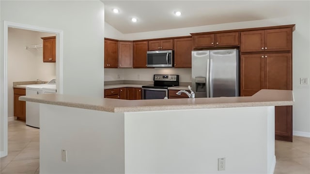 kitchen with an island with sink, light tile patterned flooring, washing machine and clothes dryer, stainless steel appliances, and vaulted ceiling