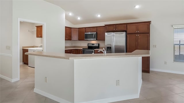 kitchen with appliances with stainless steel finishes, light tile patterned floors, lofted ceiling, washer / dryer, and a kitchen island with sink