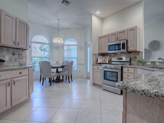 kitchen featuring light brown cabinetry, stainless steel appliances, decorative light fixtures, and sink