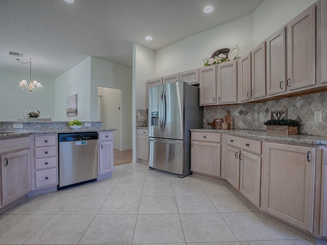 kitchen with light brown cabinets, light stone counters, a chandelier, light tile patterned flooring, and appliances with stainless steel finishes