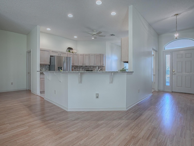 kitchen featuring a kitchen bar, stainless steel fridge with ice dispenser, light hardwood / wood-style flooring, and tasteful backsplash