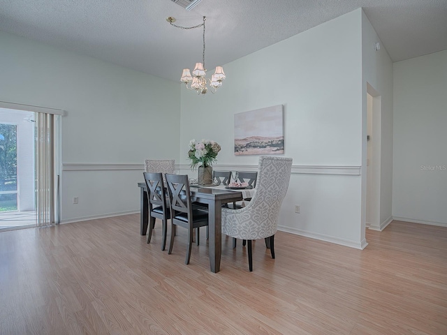 dining area featuring a textured ceiling, light hardwood / wood-style floors, and an inviting chandelier