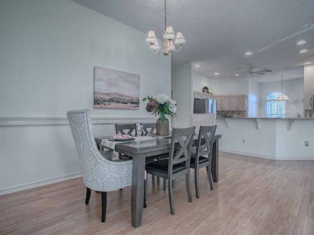 dining space with ceiling fan with notable chandelier, a textured ceiling, and light wood-type flooring