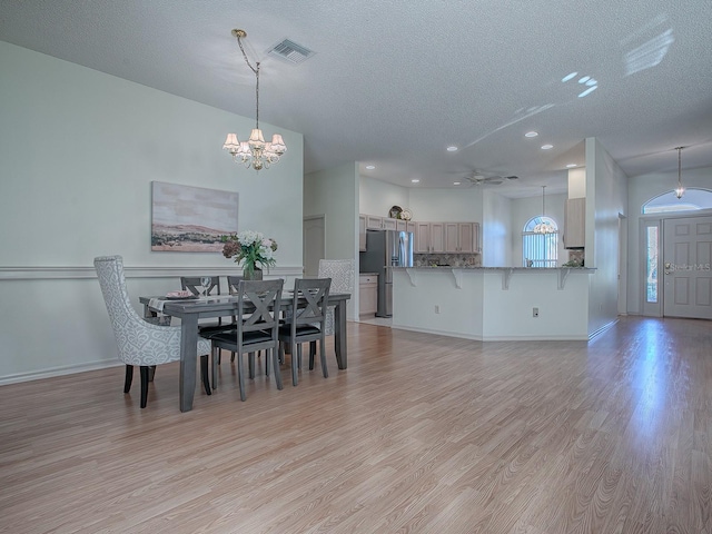 dining room with ceiling fan with notable chandelier, light hardwood / wood-style floors, and a textured ceiling