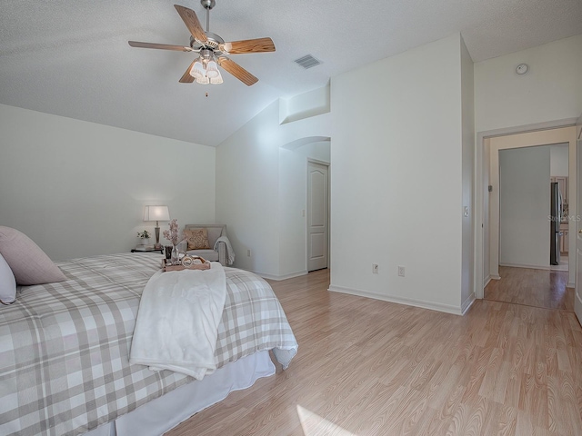 bedroom with a textured ceiling, ceiling fan, light hardwood / wood-style floors, stainless steel refrigerator, and lofted ceiling