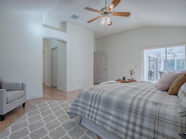 bedroom featuring ceiling fan, light hardwood / wood-style floors, a textured ceiling, lofted ceiling, and access to outside