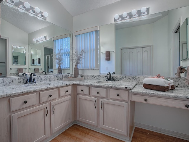 bathroom with vanity, wood-type flooring, a textured ceiling, and vaulted ceiling