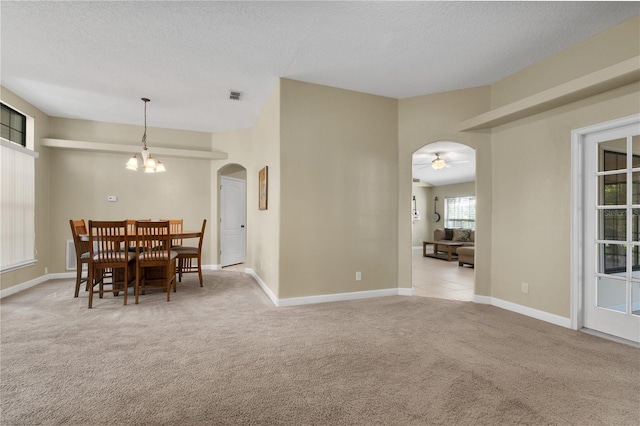 unfurnished dining area featuring a textured ceiling, ceiling fan with notable chandelier, and light carpet