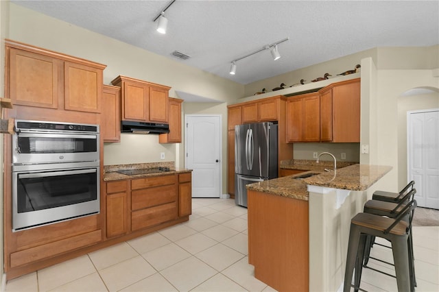 kitchen with a kitchen breakfast bar, sink, a textured ceiling, appliances with stainless steel finishes, and kitchen peninsula