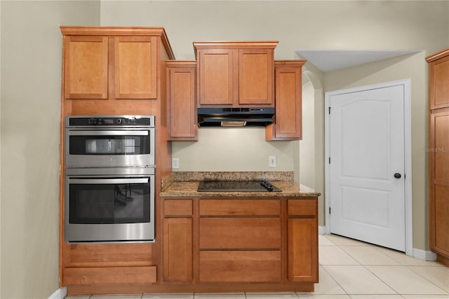 kitchen featuring black electric stovetop, light stone counters, double oven, and light tile patterned flooring