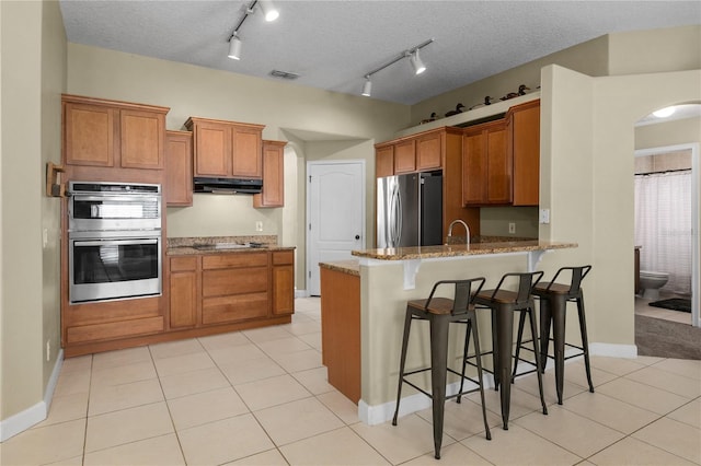 kitchen featuring kitchen peninsula, appliances with stainless steel finishes, a textured ceiling, and a kitchen breakfast bar