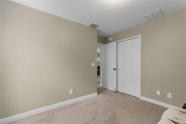 unfurnished bedroom featuring a textured ceiling, light colored carpet, and a closet