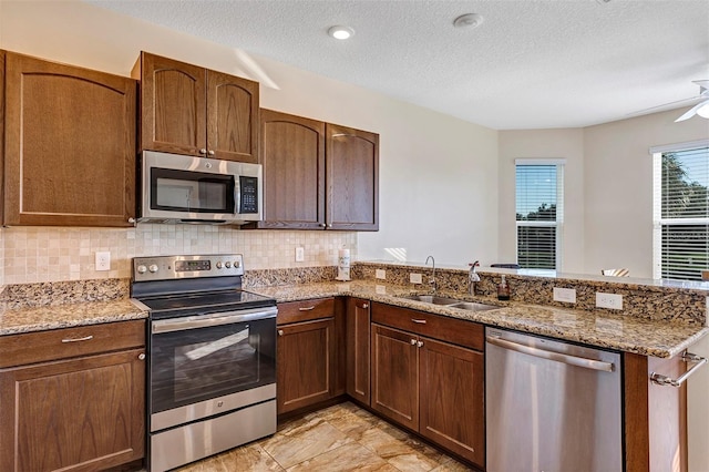 kitchen with light stone countertops, a textured ceiling, appliances with stainless steel finishes, and sink