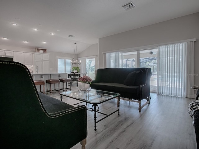 living room featuring sink, light hardwood / wood-style floors, lofted ceiling, and an inviting chandelier