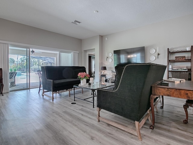 living room with ceiling fan, light hardwood / wood-style floors, and a textured ceiling