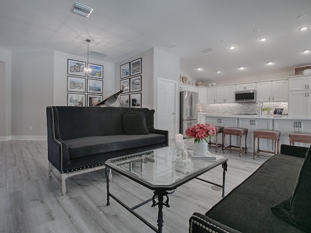 living room featuring a notable chandelier, lofted ceiling, and light hardwood / wood-style flooring