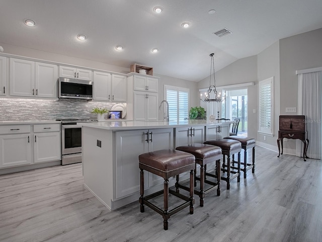 kitchen with lofted ceiling, a center island with sink, appliances with stainless steel finishes, decorative light fixtures, and a kitchen bar