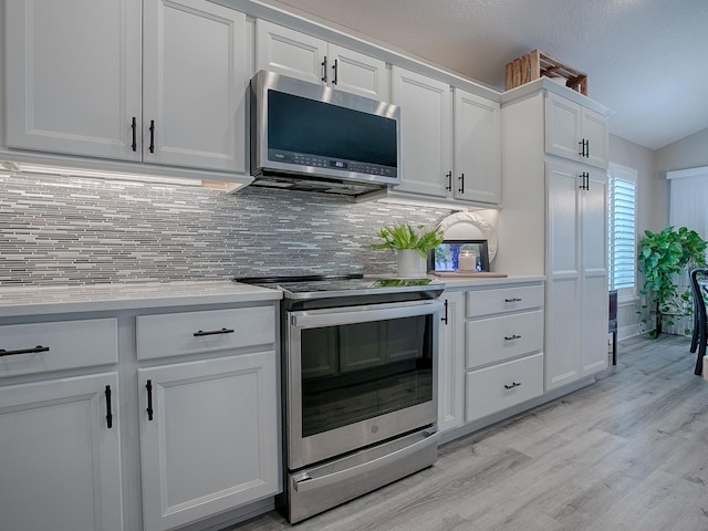 kitchen featuring appliances with stainless steel finishes, tasteful backsplash, vaulted ceiling, light hardwood / wood-style flooring, and white cabinets