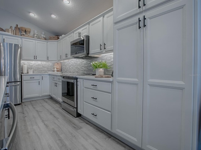 kitchen featuring appliances with stainless steel finishes, a textured ceiling, white cabinets, light hardwood / wood-style floors, and lofted ceiling