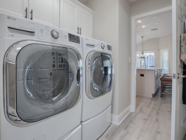 washroom featuring cabinets, light hardwood / wood-style floors, an inviting chandelier, and washing machine and clothes dryer