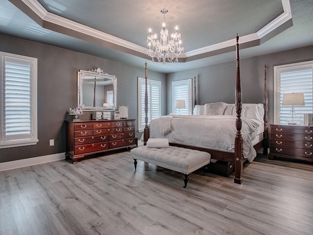 bedroom with a raised ceiling, light hardwood / wood-style flooring, ornamental molding, and a notable chandelier