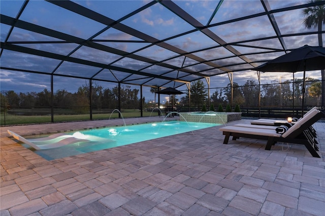 pool at dusk featuring a lanai, a patio area, pool water feature, and an in ground hot tub