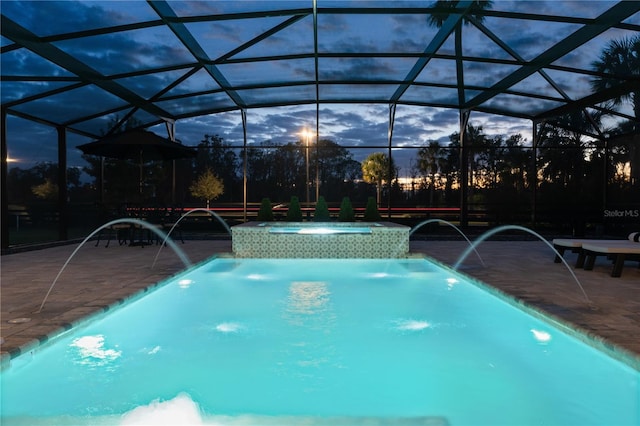 pool at dusk with glass enclosure, pool water feature, and a patio