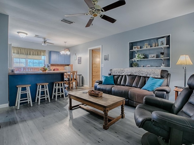 living room with ceiling fan with notable chandelier and light wood-type flooring