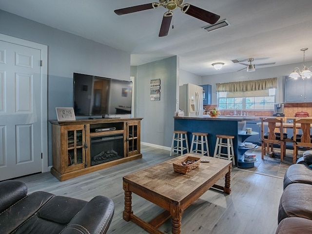 living room featuring ceiling fan with notable chandelier, light wood-type flooring, a fireplace, and sink