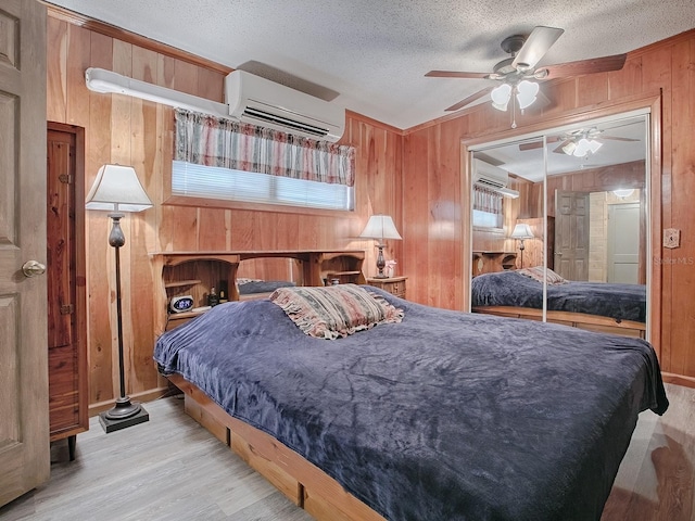 bedroom featuring wood walls, a closet, light wood-type flooring, ceiling fan, and a wall mounted air conditioner